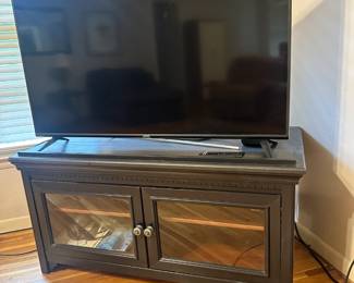TV stand with a glass-fronted cabinet and a flat-screen television 