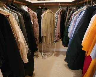 A peek at the closet full of men's clothing :  coats, suits, shirts, slacks, overcoats 