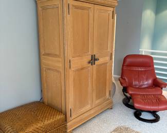 Rattan coffee table/accent piece, Wooden entertainment center, red leather accent armchair with ottoman. Beige area rug.
