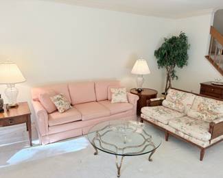 View of living room with two side tables, glass and brass coffee table, 3 cushion couch, and two cushion loveseat