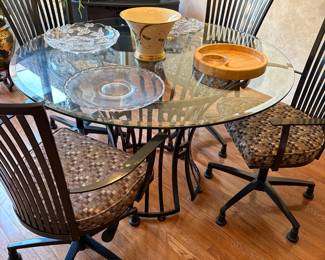 Round glass dining table with black metal base, five swivel armchairs on casters