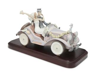 1358
A Lladro porcelain 'Honeymoon Ride' figurine
1992
Impressed: 5968; with blue inked stamp: [logo] / Lladró ® / Hand made in Spain / © Daisa / 1992; further marked indiscernibly
The glazed porcelain scene depicting a newlywed couple driving away from their wedding in a floral festooned roadster, mounted on a wood base
Porcelain without cans: 7.75" H x 14" W x 6.75" D; Overall: 8.875" H x 16.75" W x 7.75" D
Estimate: $600 - $900