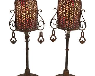 1444
A pair of Arts & Crafts Oscar Bach-style screen lamps
Early 20th century
Each unmarked
In the style of Oscar Bach (1884-1957), the bronze and wrought-iron single-light lamps with opposed hanging accents, each with purple slag glass under Moorish-style reticulated metal shade, electrified
2 pieces
Each: 23" H x 8" W x 8.25" D
Estimate: $150 - $250

