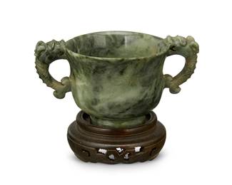 1389
A Chinese carved nephrite cup
20th century
The mottled nephrite footed cup with opposed dragon-form handles, set on a Japanese carved hardwood stand
2.25" H x 4.25" W x 2.875" D; Stand: 1" H x 2.75" Dia.
Estimate: $500 - $700