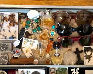 More case items: watches, perfumes, vintage European sunglasses, tiny totem pole 