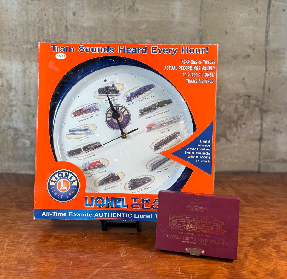 This lot features a Lionel train clock (new in box), along with a Hallmark Keepsake Ornament featuring a Lionel 700E J-1E Hudson Steam Locomotive. 
The ornament commemorates the 100th Anniversary of Lionel Trains. It is a detailed die-cast metal replica of the iconic Lionel 700E Hudson locomotive, known for its O scale detail and significance in model railroading history.