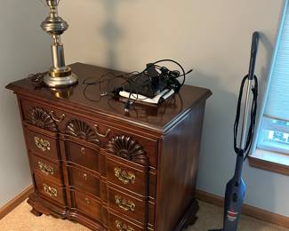 A Chippendale-style block-front chest of drawers - I believe it is made of cherry wood. On top is a brass & brushed steel hurricane-style domed table lamp. On the right is a Bissell Featherweight Stick Vacuum.