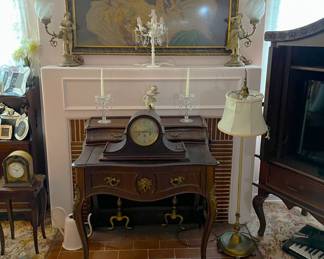 There is a mantel clock on top of the small desk in front of the fireplace.