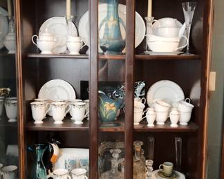 Closer view of the vintage wood carved china cabinet showing vintage barware,  Lenox Federal Platinum fine bone china plates, bowls, coffee cups, and serving pieces; Roseville Pottery Zephyr Lily Bermuda Blue handled basket, Roseville Pottery Zephyr Lily Bermuda Blue two-handled vase, antique American Brilliant Cut glass demijohn decanter with stopper, a 1950s vintage pressed glass Old Forester Kentucky bourbon whiskey bottle D-10 with cork topper, and more 