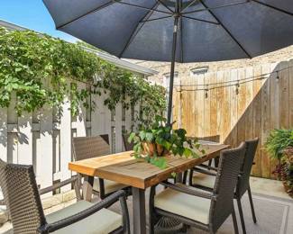 Another view of the stylish outdoor furniture including a wooden dining table with patio umbrella and a set of rattan wicker dining chairs, a large outdoor area rug, and vibrant potted plants with planters 