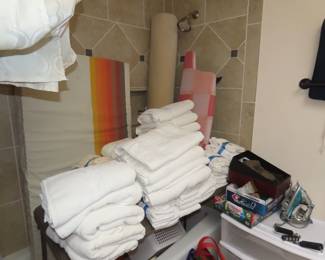 Hundreds of towels. White bathroom storage chest, plastic storage drawers, long bed bolster, iron and ironing board.