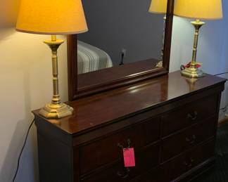 Elongated dresser with attached mirror. Pair of brass finish lamps with clean shades.