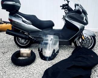  Suzuki Burgman scooter, specifically a Burgman 650 Executive. The image also shows a spare tire, an extra windscreen, and a motorcycle cover.