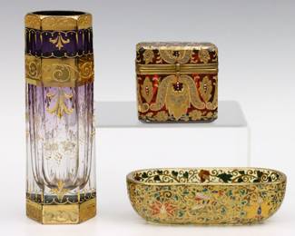 Three pieces of turn of the century Bohemian Art Glass attributed to Moser. Amethyst, Cranberry and Amber glass bodies with scrolled hand-enameled decoration and Gilded details. Includes a hexagonal vase, a hinged dresser box and an oval trinket dish with insects. Vase signed "Moser" at underside, dresser box with painted "N" and "2 2" at interior, dish unmarked. Some wear to decoration and fleabites, light scratches to undersides. Up to 6" high.