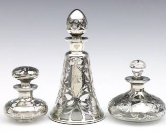 Three turn of the century Art Nouveau glass perfume bottles with Sterling Silver overlay. Various forms with floral designs. Each marked Sterling. Minor losses to overlay, some staining to interiors, tallest monogrammed. Up to 6 1/2" high.