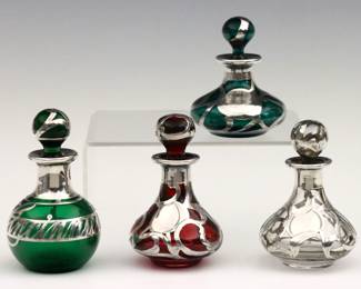 Four turn of the century Art Nouveau glass perfume bottles with Sterling Silver overlay. Various forms with clear, Ruby and Emerald Green glass bodies and scrolled designs. Each marked or tested Sterling. Clear bottle with crack to glass under Sterling overlay at rim/neck, slight staining to interiors. Up to 3 1/2" high.