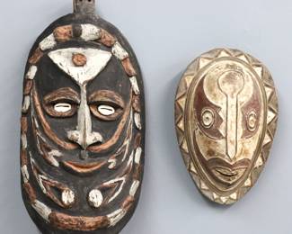 Two Papua New Guinea ceremonial masks. Carved wooden masks with polychrome decoration, includes one with cowrie shell eyes and alternating border, and a smaller one with pierced mouth and geometric border. Some wear. Up to 19 1/2" high.
