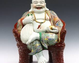 A large Chinese Famile Rose porcelain figure of a Laughing Buddha. Depicted seated in a "carved" armchair with scenic panels, holding a cloth sack representing his origin as the monk Budai in one hand, and an small Gilded bowl representing wealth and prosperity in the other. Some wear to enameled decoration particularly at belly, some areas with craquelure. Approx. 15 x 14 x 21" high overall.