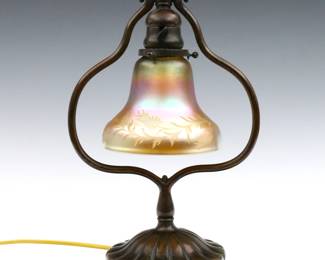 An early 20th Tiffany desk lamp with Steuben Art Glass shade. Adjustable patinated Bronze harp base with circular foot and a bell form glass shade with etched floral decoration and Iridescent Gold finish. Base double impressed "Tiffany Studios / New York" and "419", shade with partial Steuben Fleur des Lis mark at fitter. Minor wear, some tiny flakes at fitter. Shade is 4 3/4" high with 2" fitter, 13 1/2" high overall.