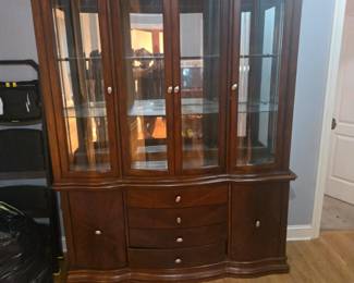 Beautiful dark wood china cabinet with glass display doors, interior lighting, and ample storage, including drawers and side compartments. Excellent condition. Approx. 78"H x 60"W x 17"D.