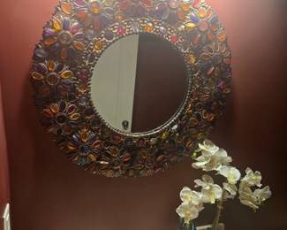 Round mirror with ornate jeweled frame featuring vibrant glass stones in amber, purple, and ruby hues. Adds color and elegance to any bathroom or entryway. Approx. 24" diameter.