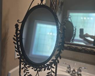 Antique-style oval tabletop vanity mirror with wrought iron frame and scroll detailing. Tilts for adjustable viewing. Approx. 20” H x 12” W.