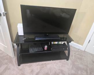 Modern black glass TV stand with metal frame, featuring two lower shelves for storage or media equipment. Clean lines with a contemporary finish.
Approx. 42”W x 18”D x 22”H.