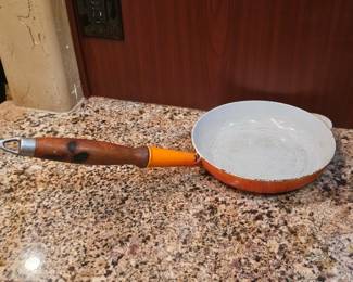 cast iron skillet with an enameled interior, a wooden handle, and an orange exterior.
