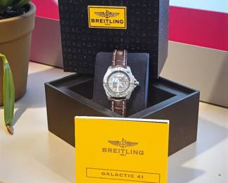 Authentic Breitling men’s wristwatch featuring a black dial, date window, and rich brown alligator-style leather band. Includes original presentation box, warranty card, and booklet. Watch shows light surface wear consistent with gentle use.