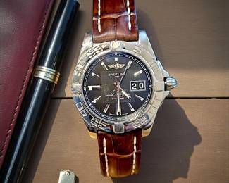 Authentic Breitling men’s wristwatch featuring a black dial, date window, and rich brown alligator-style leather band. Includes original presentation box, warranty card, and booklet. Watch shows light surface wear consistent with gentle use.