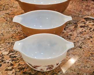 vintage Pyrex "Early American" Cinderella mixing bowls. These bowls are characterized by their brown color and a repeating pattern of various early American motifs, such as eagles, lamps, and weathervanes. 
The set includes four nesting bowls, with sizes ranging from 1.5 pints to 4 quarts. 
The bowls are made of glass and were manufactured in the United States. 
The "Cinderella" name comes from the design, which features a handle or spout on each side of the bowl. 
The bowls are sold seperately 
