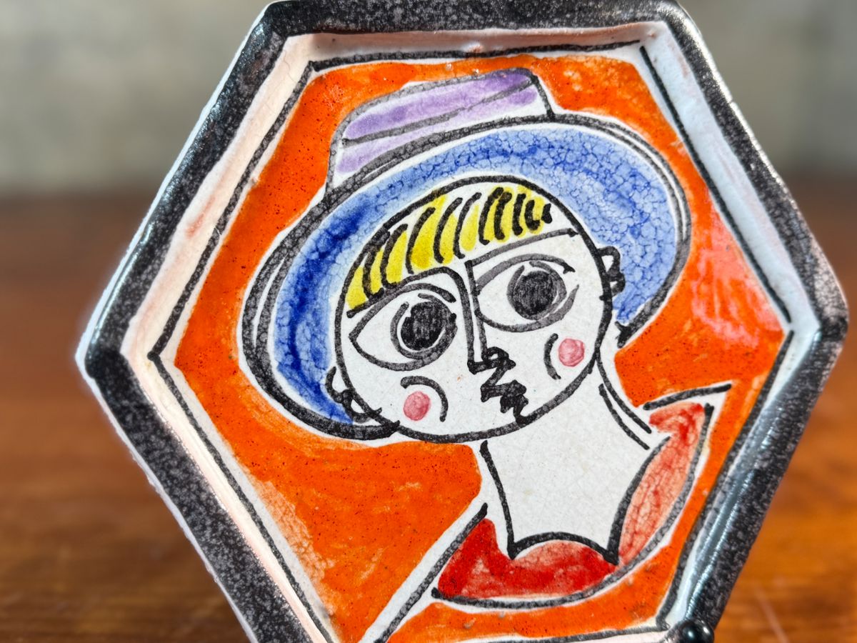 This lot features a stunning hand-painted hexagonal ceramic plate by listed Italian artist, Giovanni De Simone, circa 1960s. This piece measures, 6.25” H x 7” W. De Simone’s work is known for its vibrant colors and cubist drawing style, which was influenced by artists like Pablo Picasso. The company’s artistic tradition is continued by his daughter, Susanna De Simone. 
