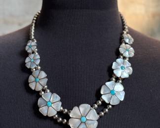This lot features a vintage Zuni Native American squash blossom necklace, made of sterling silver with mother-of-pearl and turquoise inlay with a floral design. This necklace measures 24” and has a total approx. weight of 134.87 grams.
