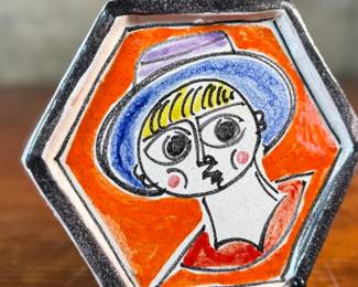 This lot features a stunning hand-painted hexagonal ceramic plate by listed Italian artist, Giovanni De Simone, circa 1960s. This piece measures, 6.25” H x 7” W. De Simone’s work is known for its vibrant colors and cubist drawing style, which was influenced by artists like Pablo Picasso. The company’s artistic tradition is continued by his daughter, Susanna De Simone.