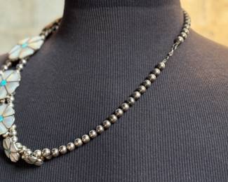 This lot features a vintage Zuni Native American squash blossom necklace, made of sterling silver with mother-of-pearl and turquoise inlay with a floral design. This necklace measures 24” and has a total approx. weight of 134.87 grams.
