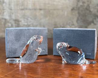 This lot features a set of two Steuben Crystal beaver figurines with garnet eyes, designed by Lloyd Atkins for Steuben in 1975. Comes with a pair of Steuben boxes. 

