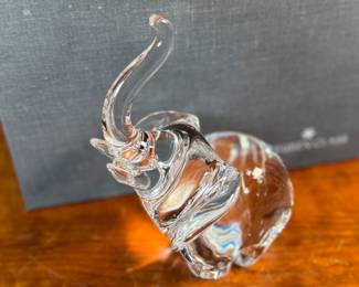 This lot features a Steuben crystal elephant with a raised trunk, designed by James Houston in 1964. Comes with a Steuben box for storage.
