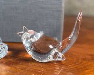 This lot features a collection of three (3) animal themed Steuben Glass sculptures, with five cases to accompany them. Steuben Glass is an American art glass company founded in Corning, New York, in 1903 by Frederick Carder. Originally known for colored glass, it shifted to brilliant clear crystal in the 1930s after being acquired by Corning Glass Works (now Corning Inc.) in 1918. The brand was sold in 2008, production ceased in 2011, and was reacquired by Corning Inc., which now oversees its production and sales through the Corning Museum of Glass.
