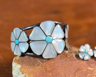 This lot features a vintage set of Zuni Native American jewelry including a bracelet cuff, earrings, and a ring made of sterling silver. The cuff has one inlay piece missing as shown in photos. The ring is a size 5, and the set has a total approx. weight of 57.05 grams. 
