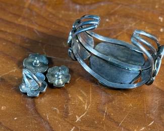 This lot features a vintage set of Zuni Native American jewelry including a bracelet cuff, earrings, and a ring made of sterling silver. The cuff has one inlay piece missing as shown in photos. The ring is a size 5, and the set has a total approx. weight of 57.05 grams. 
