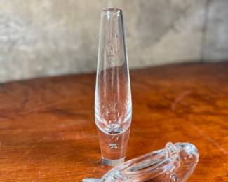 This lot features a collection of four (4) animal themed Steuben Glass sculptures along with one tall skinny Steuben Glass vase, with with Steuben sleeves to accompany them. Steuben Glass is an American art glass company founded in Corning, New York, in 1903 by Frederick Carder. Originally known for colored glass, it shifted to brilliant clear crystal in the 1930s after being acquired by Corning Glass Works (now Corning Inc.) in 1918. The brand was sold in 2008, production ceased in 2011, and was reacquired by Corning Inc., which now oversees its production and sales through the Corning Museum of Glass.
