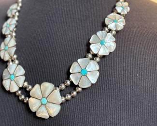 This lot features a vintage Zuni Native American squash blossom necklace, made of sterling silver with mother-of-pearl and turquoise inlay with a floral design. This necklace measures 24” and has a total approx. weight of 134.87 grams.
