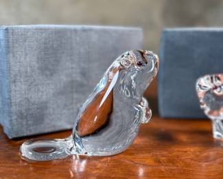 This lot features a set of two Steuben Crystal beaver figurines with garnet eyes, designed by Lloyd Atkins for Steuben in 1975. Comes with a pair of Steuben boxes. 

