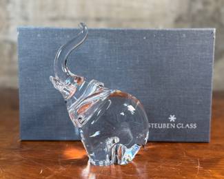 This lot features a Steuben crystal elephant with a raised trunk, designed by James Houston in 1964. Comes with a Steuben box for storage.
