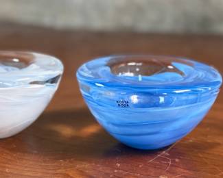 This lot features a set of Kosta Boda Atoll glass votive candle holders, designed by Anna Ehrner, with a white swirl and a blue swirl pattern. Anna Ehrner, born 1948 in Danderyd in Stockholm, is both a designer and glass artist who’s characterized by her simple design language. With an experimental expression, she has an ability to create effectful pieces with only a little color, where lines of color inside the glass has become a recurring feature.
