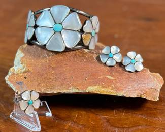 This lot features a vintage set of Zuni Native American jewelry including a bracelet cuff, earrings, and a ring made of sterling silver. The cuff has one inlay piece missing as shown in photos. The ring is a size 5, and the set has a total approx. weight of 57.05 grams. 
