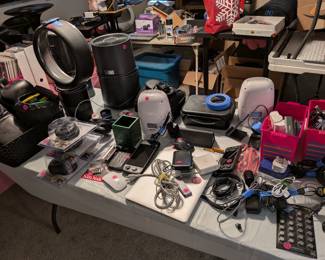 Electronics and Tech Accessories Display Table
White folding table loaded with various electronics including air purifiers, fans, gaming controllers, SanDisk storage, cables, and tech accessories. Consumer electronics, tech gadgets, gaming accessories.