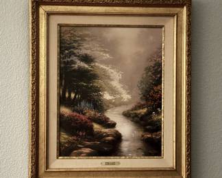 Painting in a gold ornate frame depicting a serene forest stream landscape with trees and colorful shrubbery. The back of the canvas is signed with sketches and inscriptions including 'The Path to Home' and has a wire for hanging. There is a gold plaque on the frame stating 'The Thomas Kinkade Limited Edition Hand-Crafted with Pride for the Lighthouse Publication Collectors'. Additional labels and certificates are attached to the wooden stretcher frame.