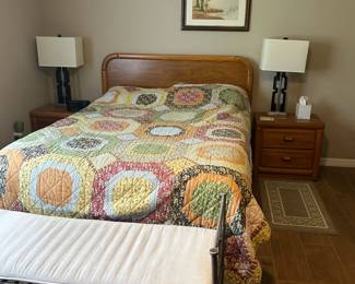 Queen-size bed with oak headboard and matching nightstands. Iron bench with cream-colored cushion