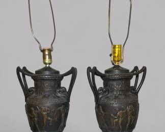 Pair Of Neoclassical Style Bronze Painted Metal Two Handled Urns On Marble Bases, Now As Lamps, having dancing figural relief and swan head handles on a marble base, Urn: H: 16 x w: 9 inches, Lamp H: 29 1/2 inches (to the finial)
